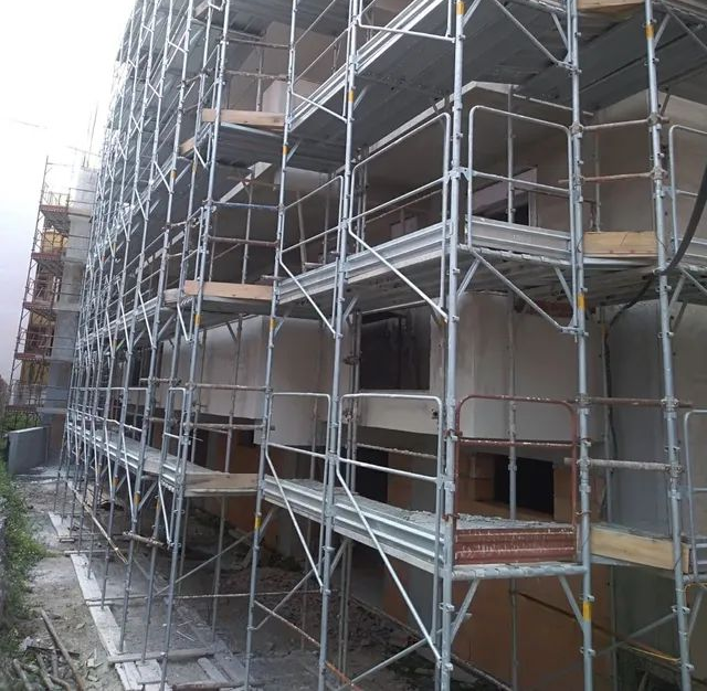 Edificio multipiano in costruzione, con impalcature, cemento a vista e finestre aperte.