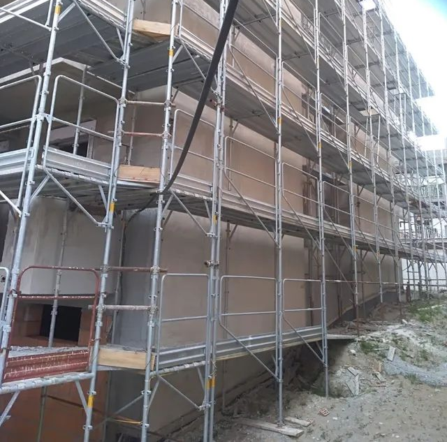 Impalcature attorno a un edificio incompiuto con pannelli murali marroni in un cantiere.