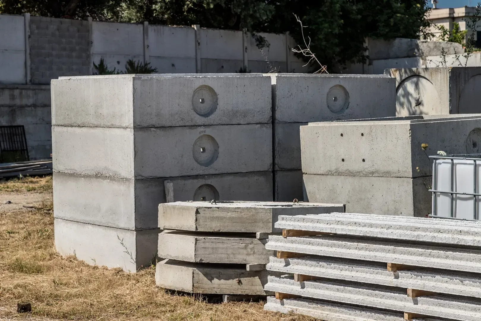 Pile di mattoni di argilla rossa disposte all'aperto in un cortile, addossate a un muro di cemento.