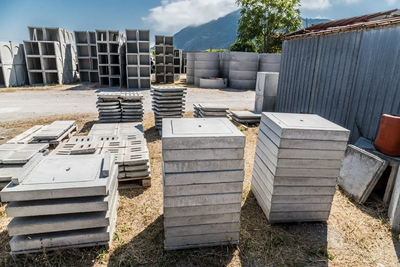 Pile di lastre di cemento grigio in un piazzale industriale all'aperto, accanto a una recinzione blu ondulata.