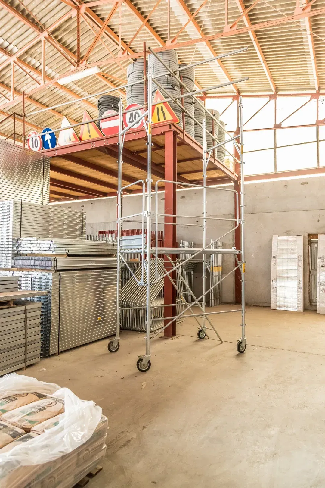 Ponteggio all'interno di un magazzino con soppalco in legno e materiali accatastati sotto un tetto alto.