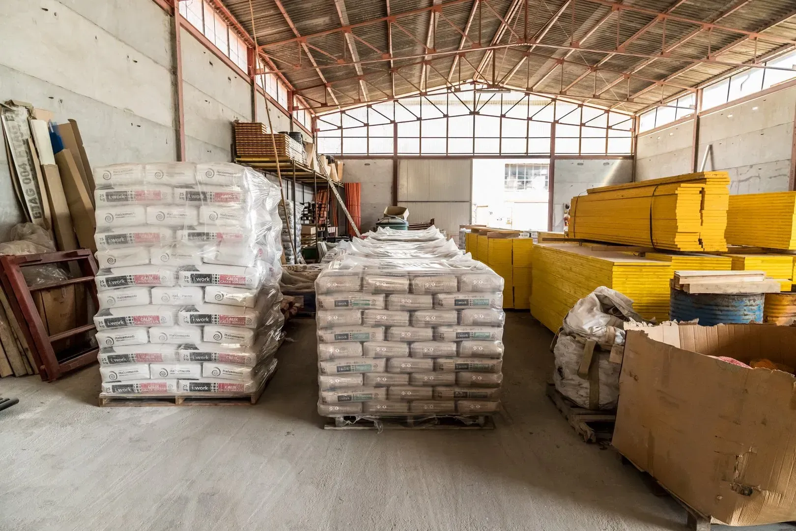 Pallet di materiale edile insacchettato impilati in un'area di stoccaggio di un magazzino.