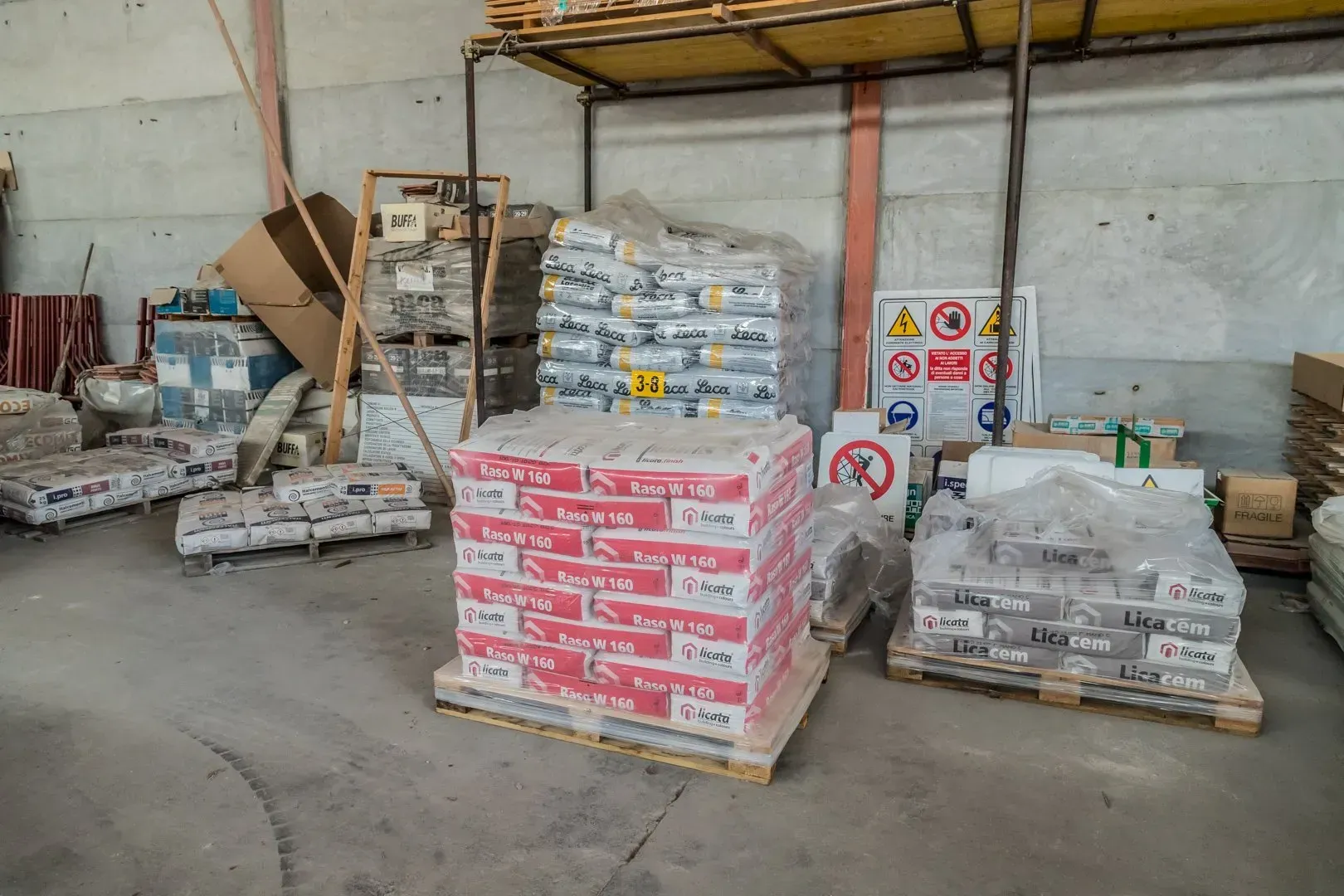 Una betoniera turchese in un'officina, circondata da blocchi impilati e attrezzi.