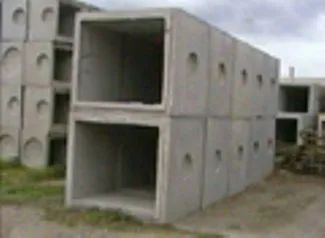 Blocco di cemento bianco a forma di cubo con fori laterali circolari, posizionato all'aperto su ghiaia.