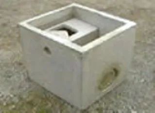 Due piccole strutture in blocchi di cemento grigi con aperture ad arco, ciascuna accanto a una pietra quadrata su una superficie ruvida