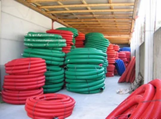 Rimorchio di un camion carico di pile di tubi flessibili o rigidi arrotolati, di colore verde e rosso.