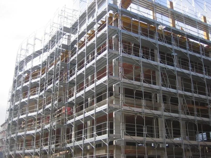 Ponteggi che circondano un edificio a più piani in costruzione, con cemento e struttura metallica a vista.