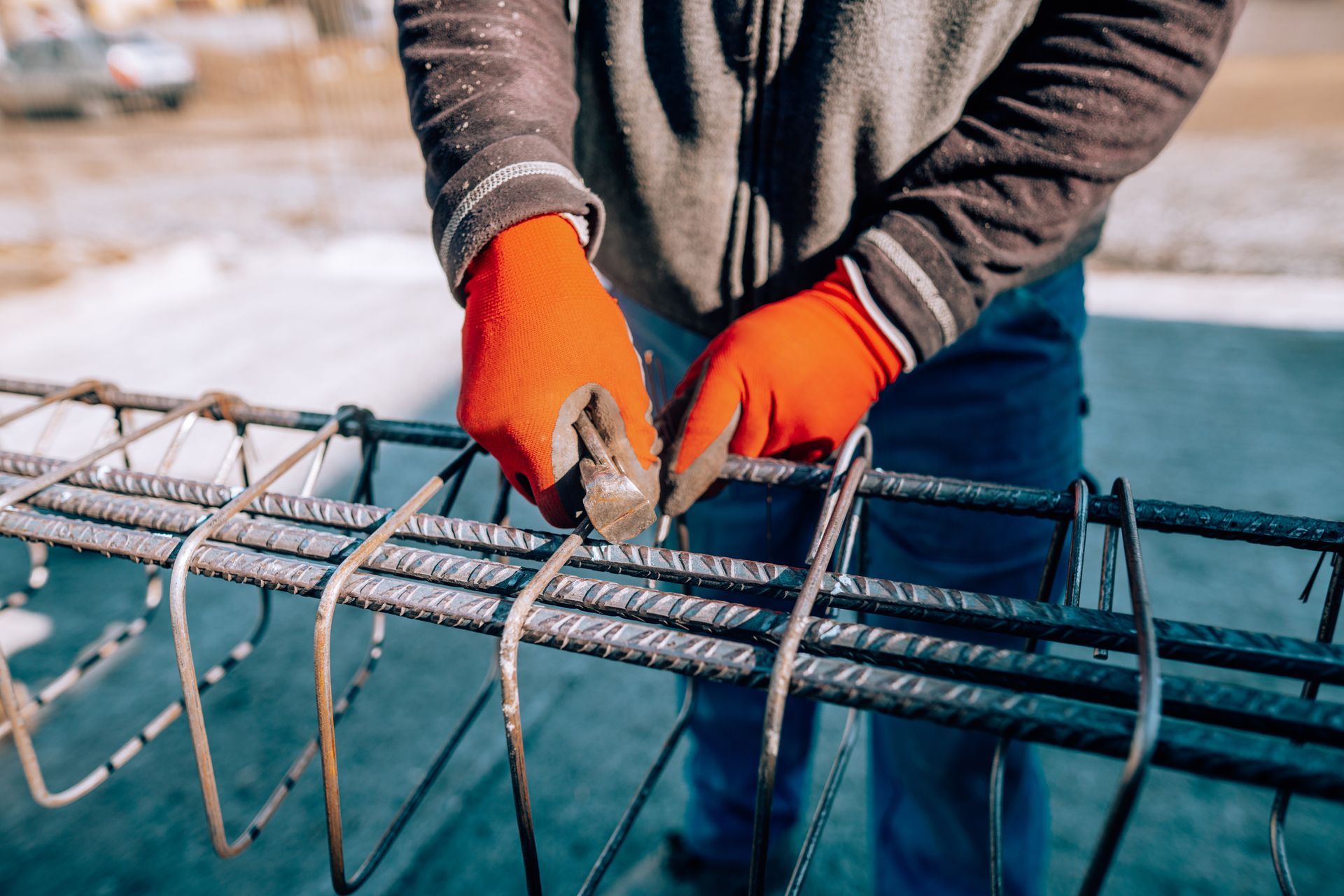 Des mains gantées d'orange attachent des barres d'armature avec du fil de fer sur un chantier de construction près de l'eau