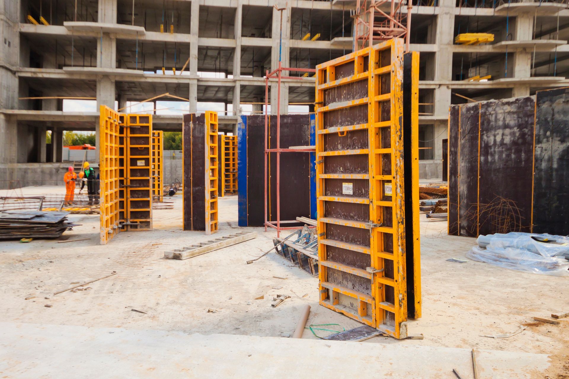 Chantier de construction avec panneaux de coffrage orange et supports muraux en béton à l'intérieur d'une ossature de bâtiment