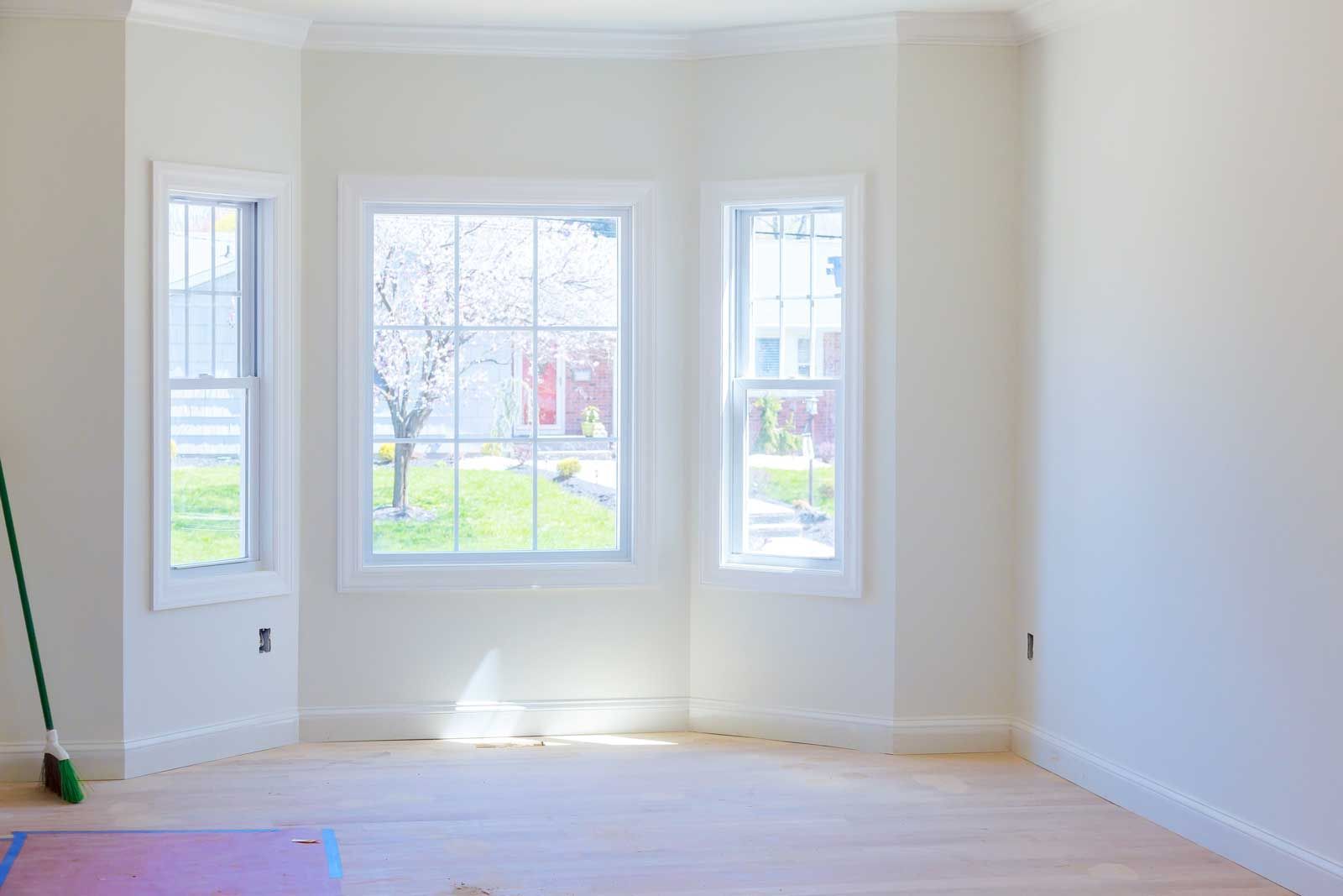 Bright empty room with white walls, bay windows, and light wood floors, lit by daylight