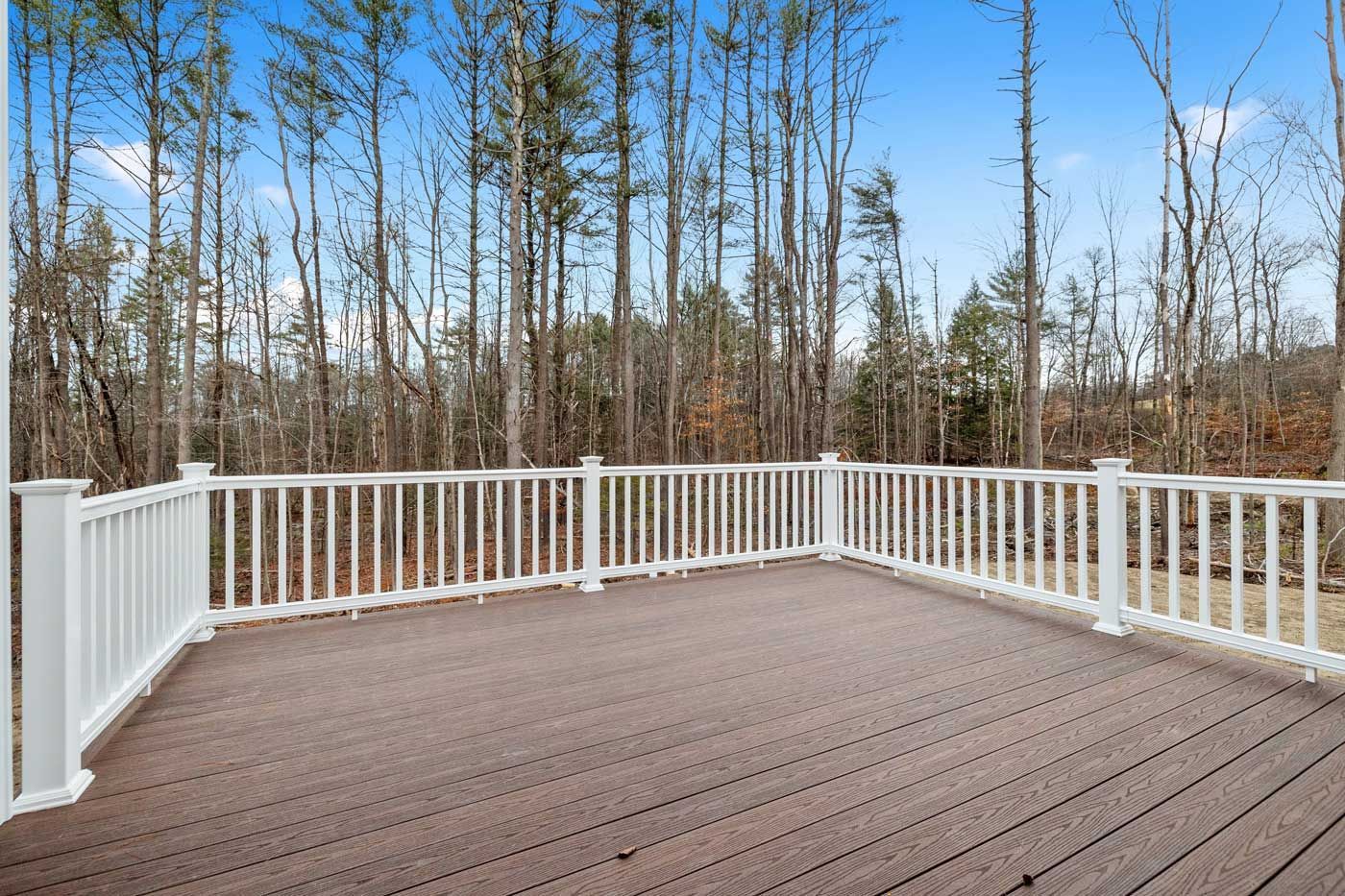 Spacious brown deck with white railing overlooking leafless trees under a blue sky