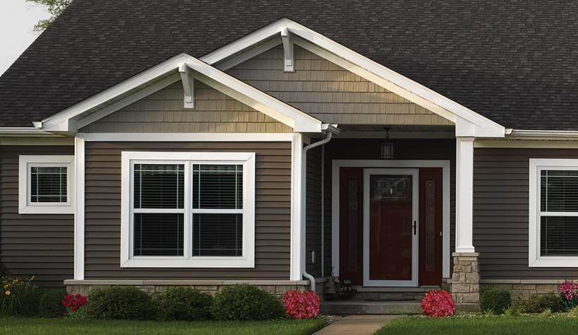 Single-story house with gray siding, white trim, and a red front door surrounded by shrubs.