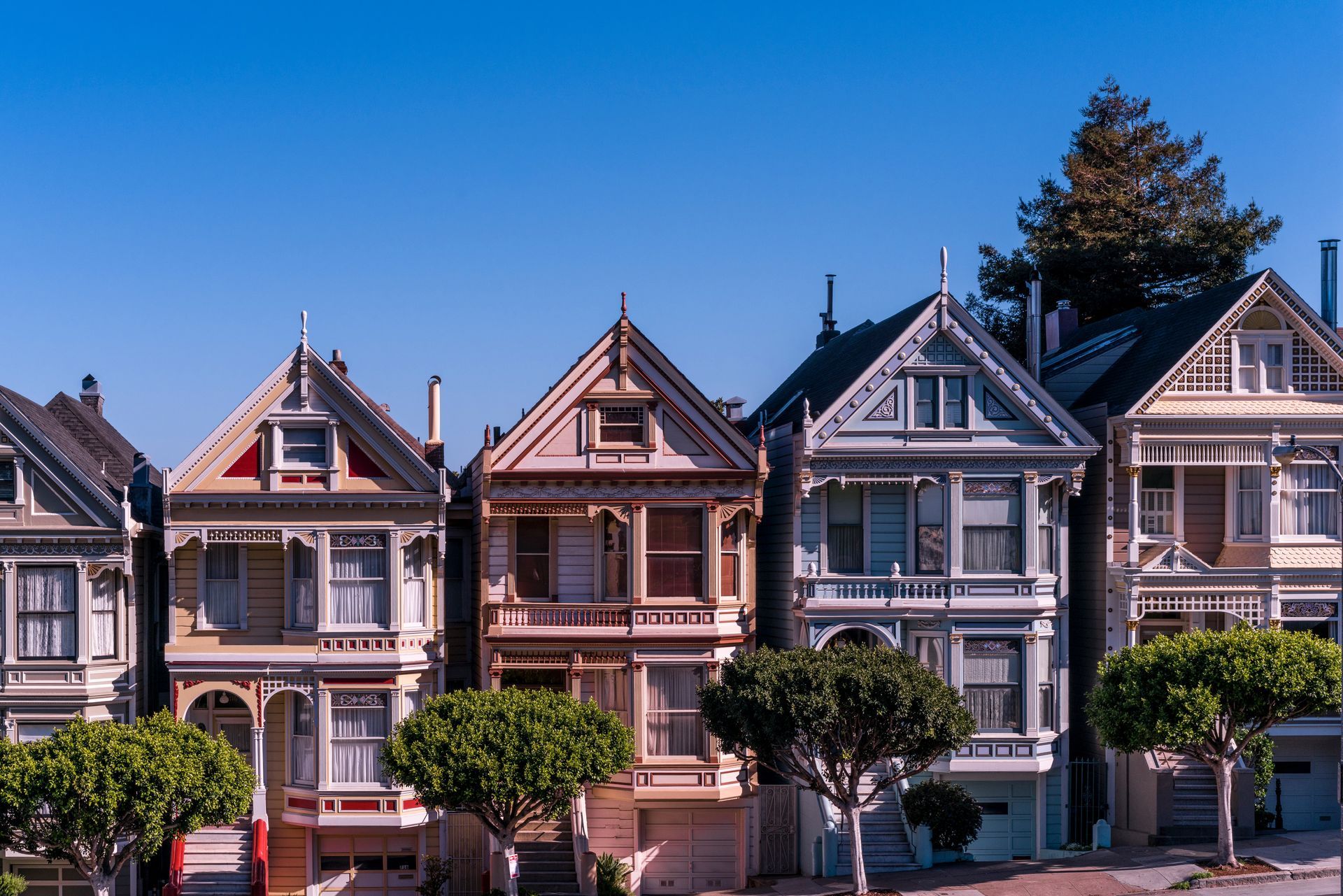 Row of colorful Victorian houses with ornate facades and small trees in front