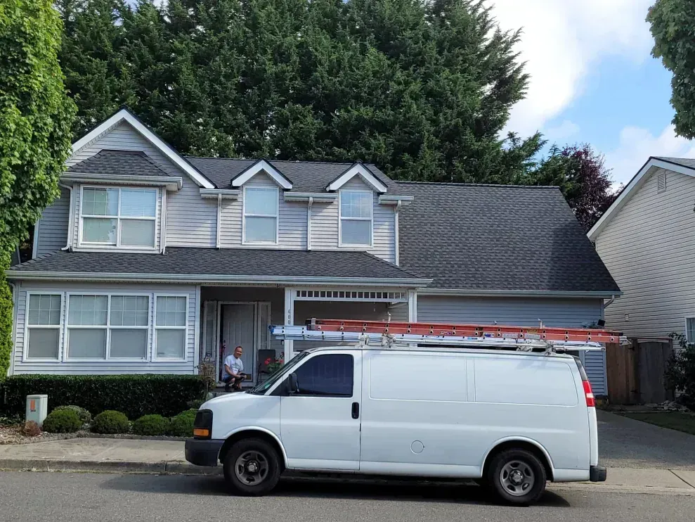 White work van parked in front of a two-story suburban house with gray siding and a garage
