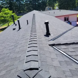 Rooftop with gray shingles, multiple vent pipes, and a ridge vent under bright sunlight