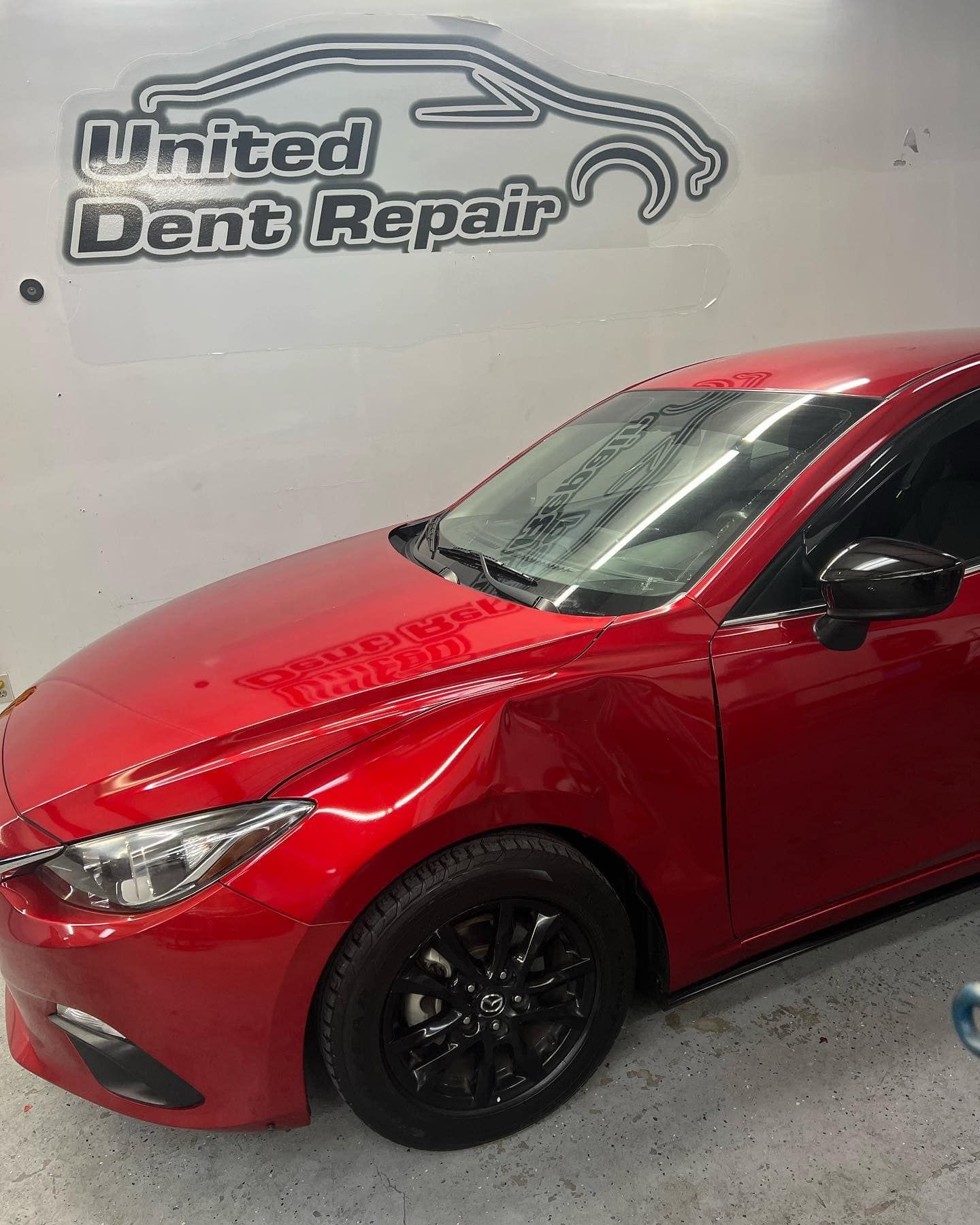 Red car in a body shop with a United Dent Repair sign on the wall