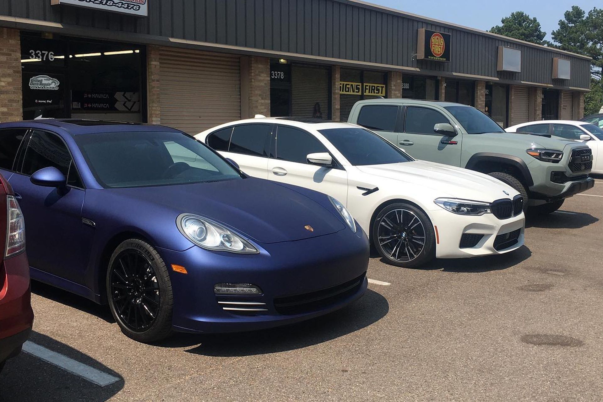 Parked sports cars outside a storefront, including a purple car and white car in front