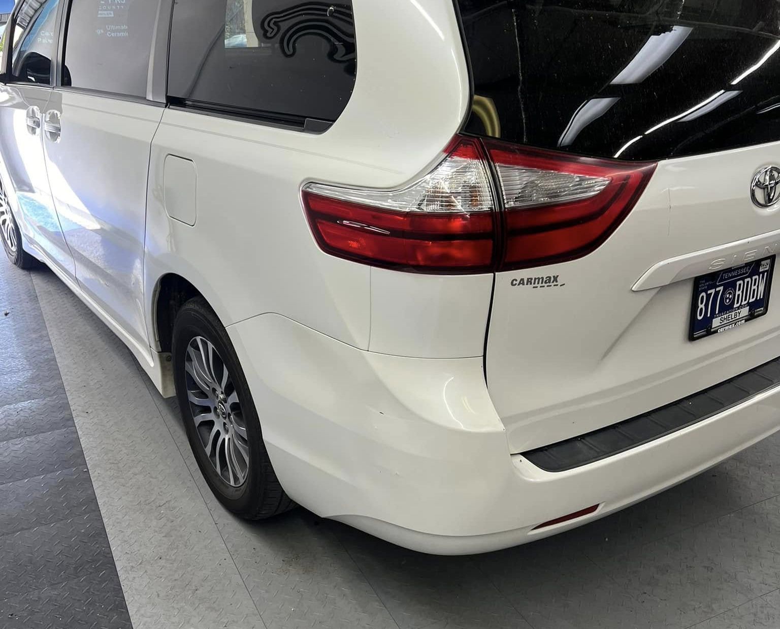White Toyota minivan parked in a garage, rear three-quarter view.