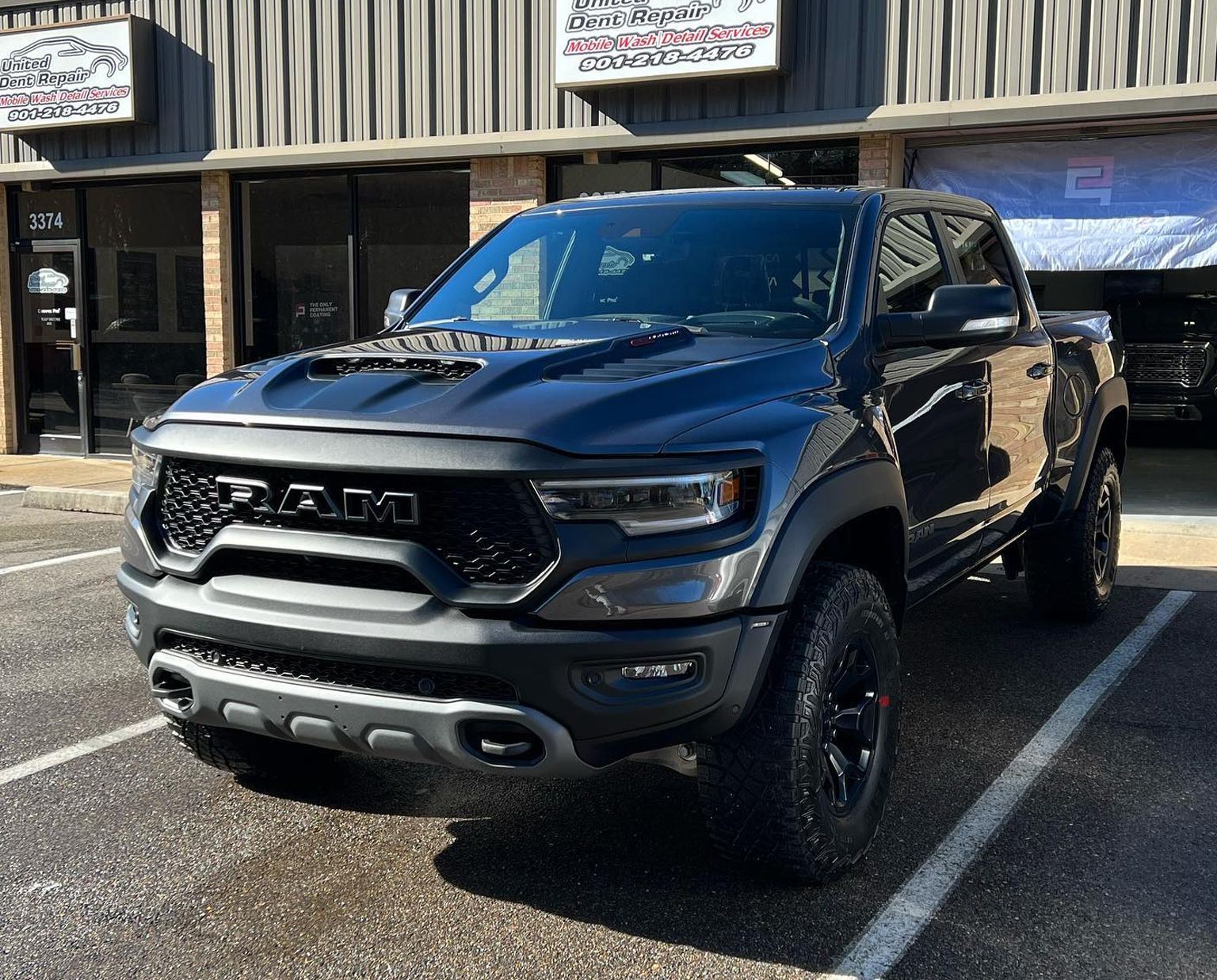 Dark gray pickup truck parked outside a storefront in daylight