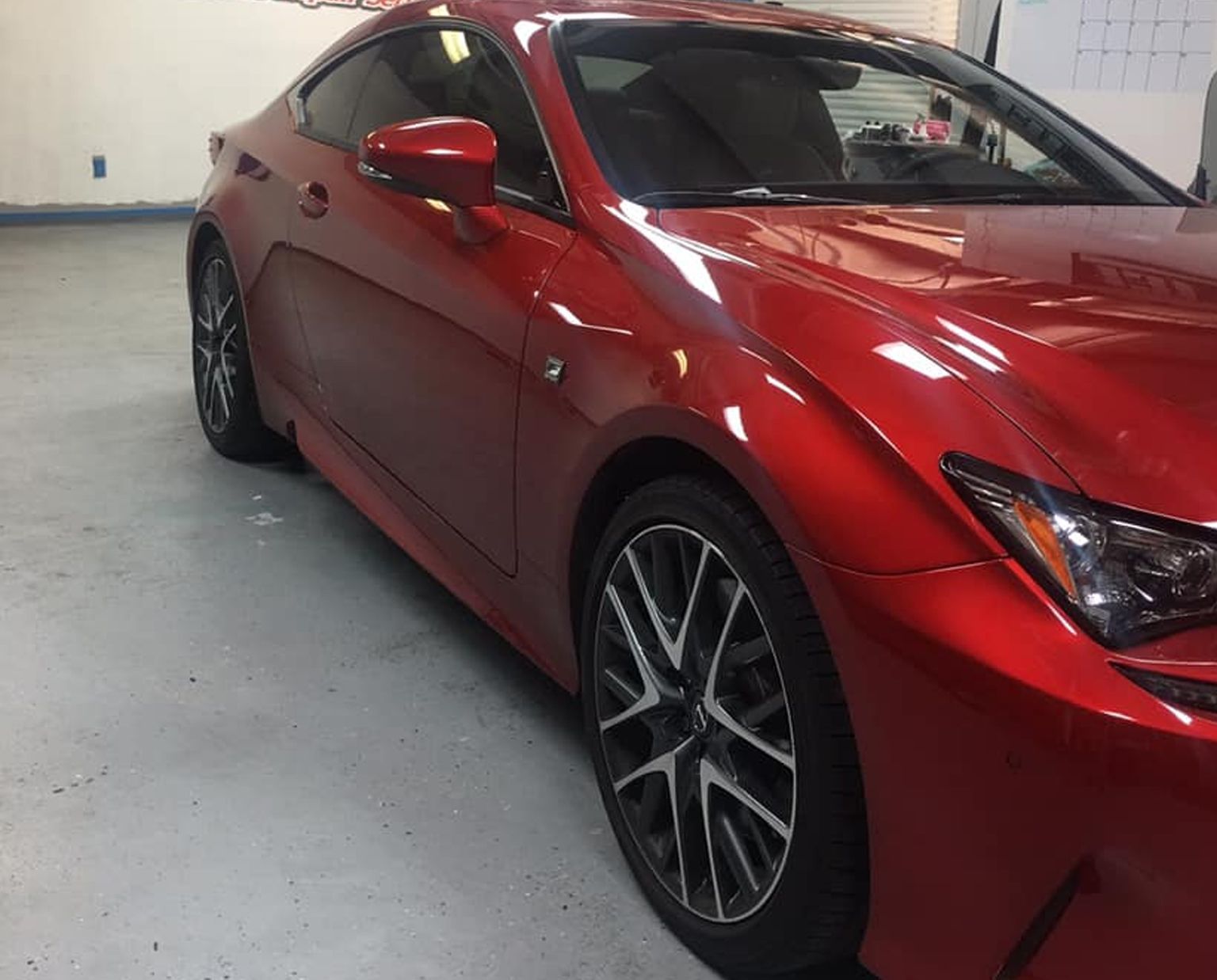 Red sports coupe in a garage, shown from the front side with glossy paint and alloy wheels
