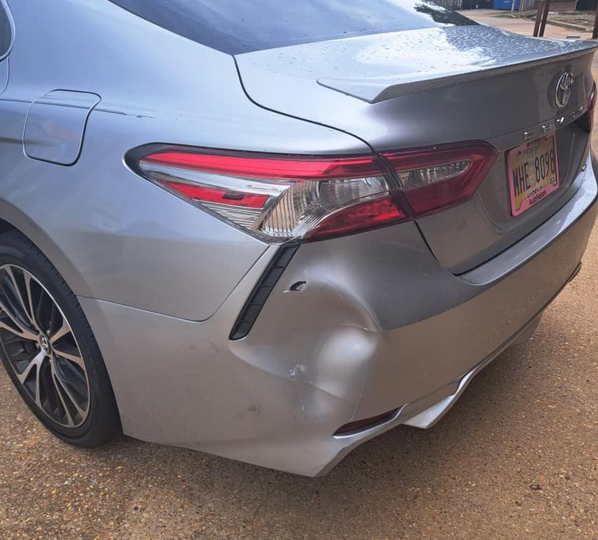 Rear-left view of a silver sedan with a dented bumper and damaged taillight.