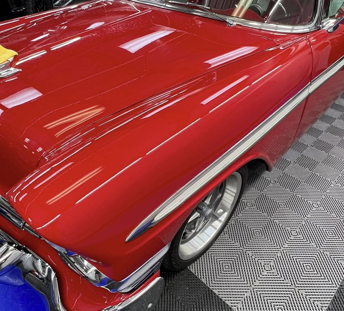 Shiny red classic car hood and front fender displayed on a showroom floor