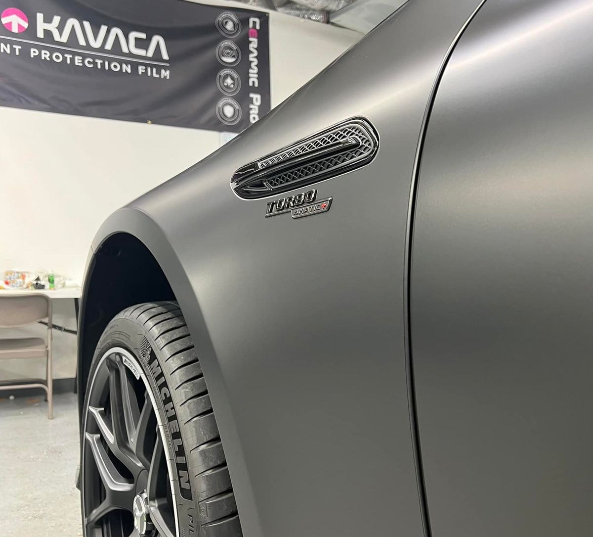 Matte gray sports car close-up in a garage, showing front wheel and side fender