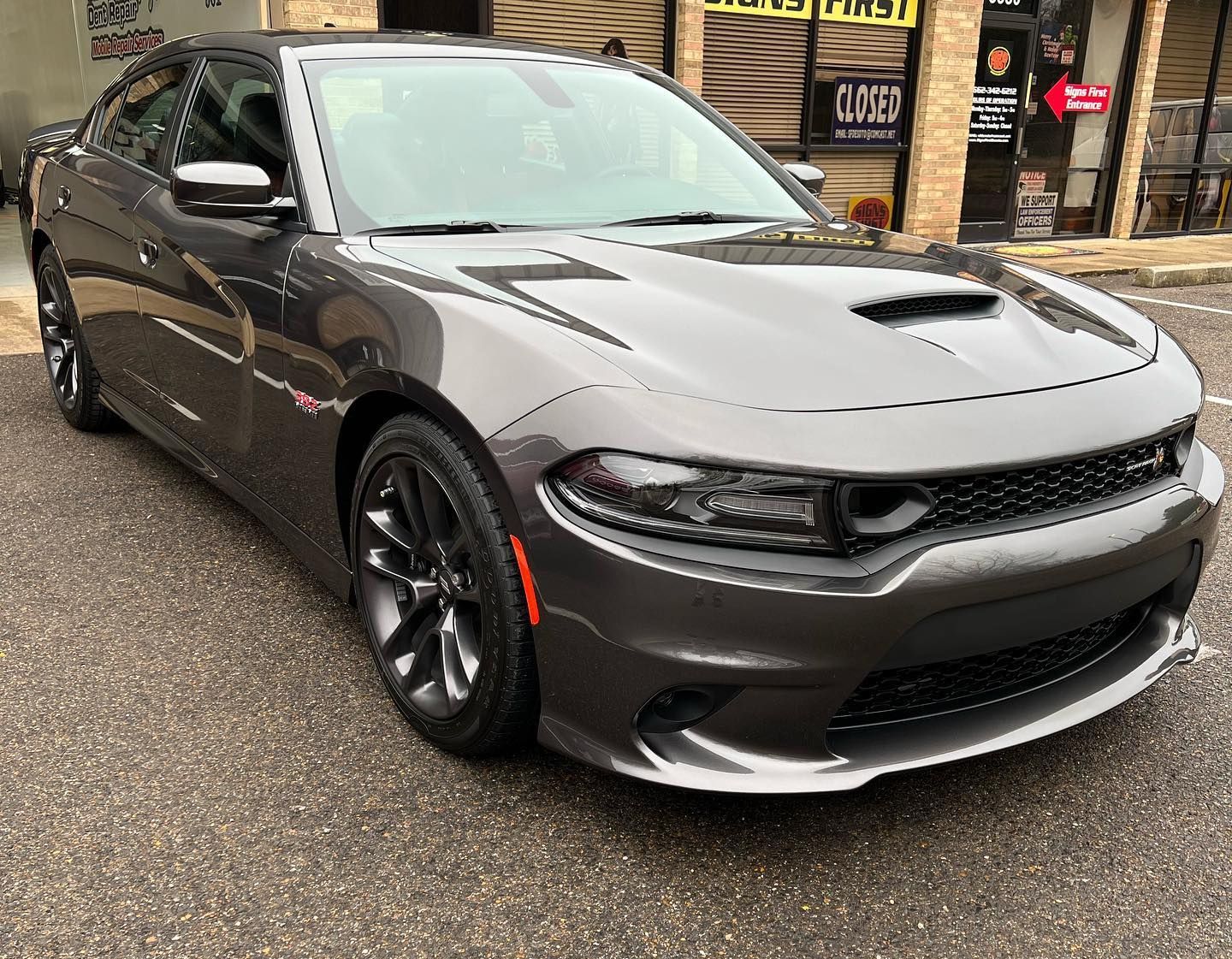 Gray sports sedan parked on a wet street outside a shop, front three-quarter view