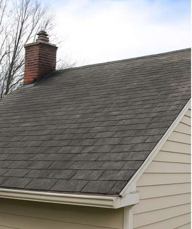 A house roof with a brick chimney and gutter, set against a cloudy sky.