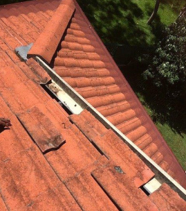 Orange tile roof with a white gutter, damaged tiles.
