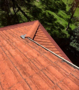 Red tile roof with a metal channel, angled view, green trees in background.