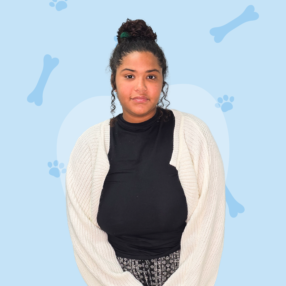 A woman wearing a black shirt and a white sweater is standing in front of a blue background with bones and paw prints.