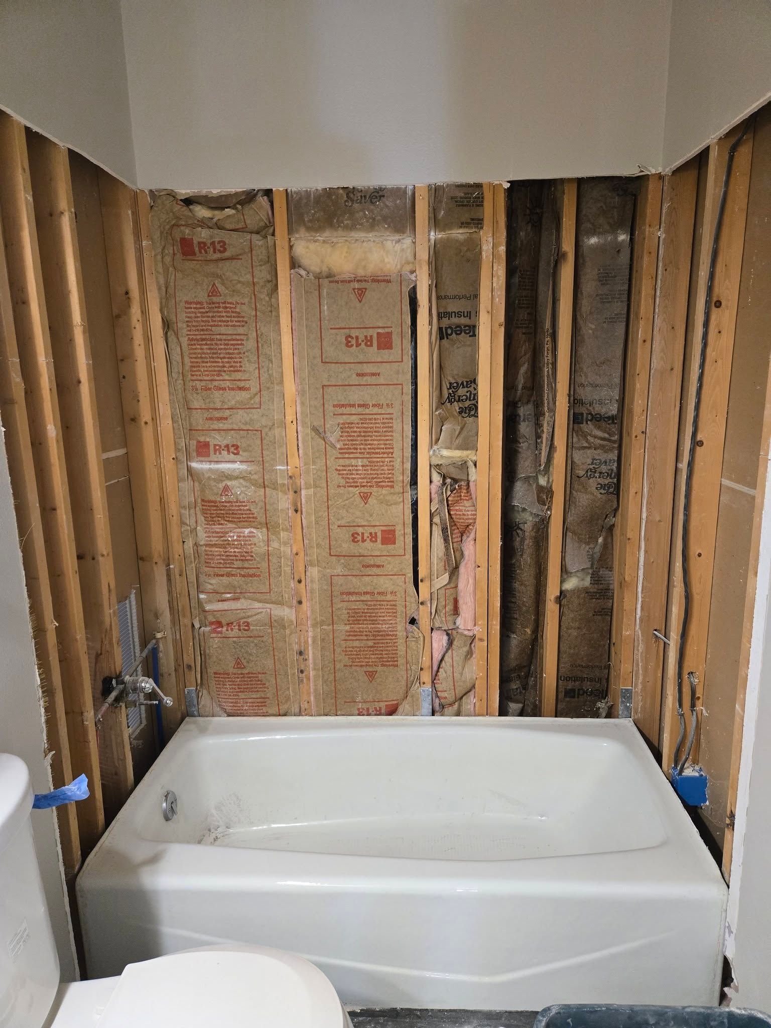 Partially renovated bathroom with a white bathtub set against exposed wall studs and insulation.