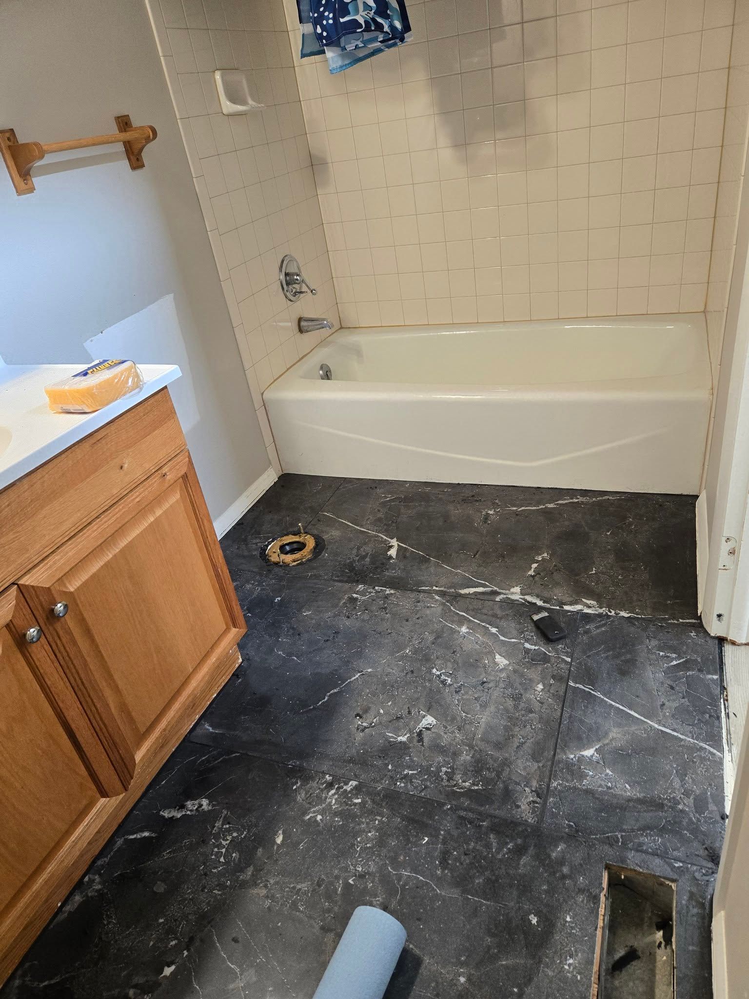 Partially renovated bathroom with tub, vanity, exposed subfloor, and dark debris-covered flooring