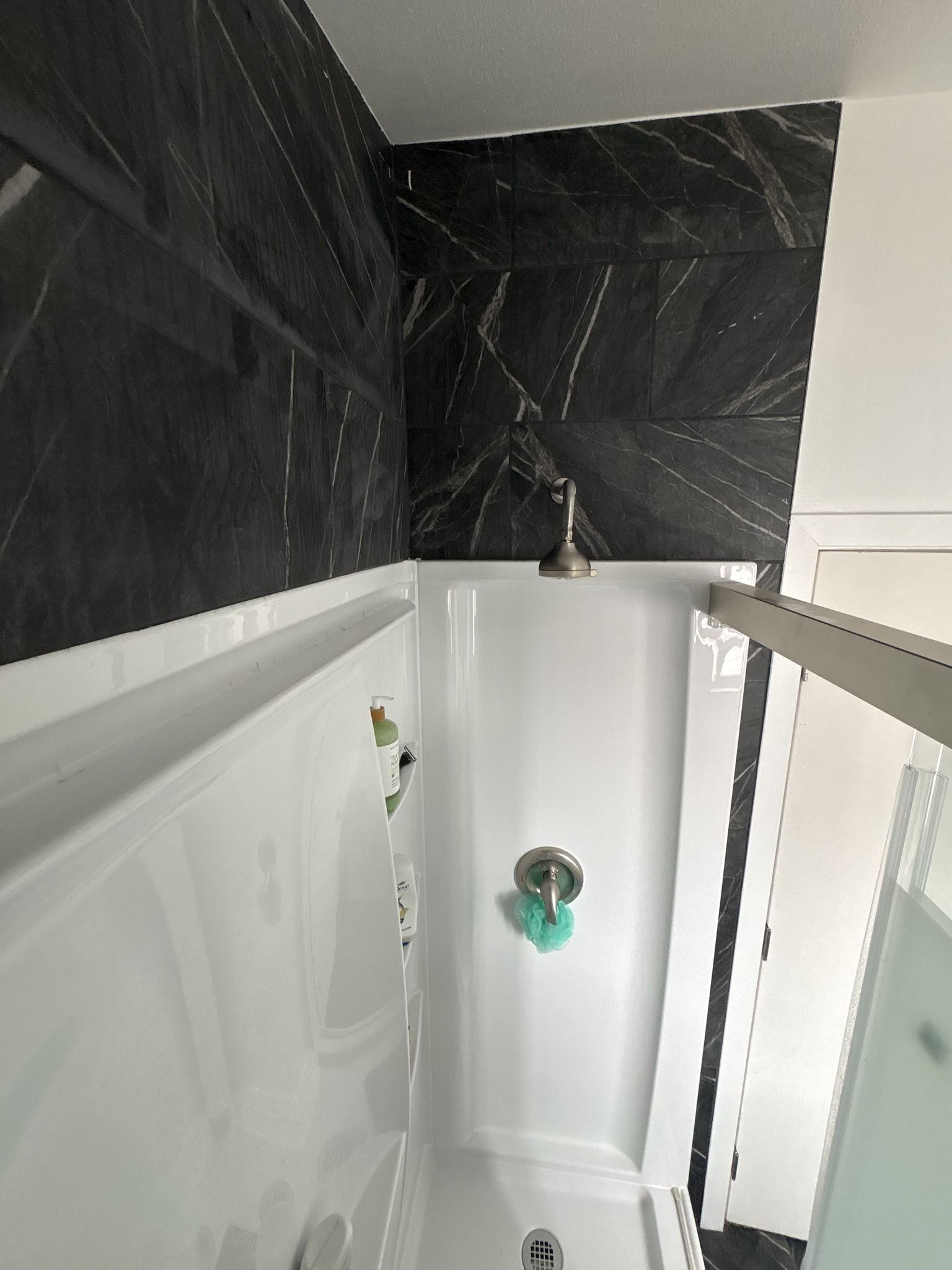 Small bathroom shower with black tile walls, white shower pan, and glass enclosure.
