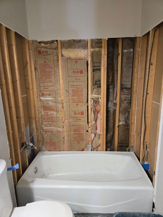 Bathtub in a bathroom under renovation with exposed studs and insulation on the walls