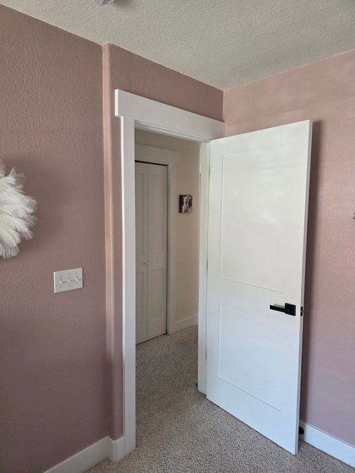 Pink bedroom with open white door and white trim, showing a hallway beyond.
