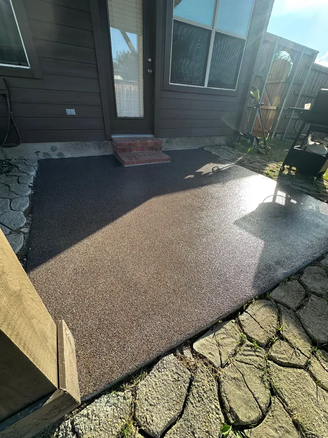 Concrete patio with brown speckles, next to a backyard with a door and stamped stone border.
