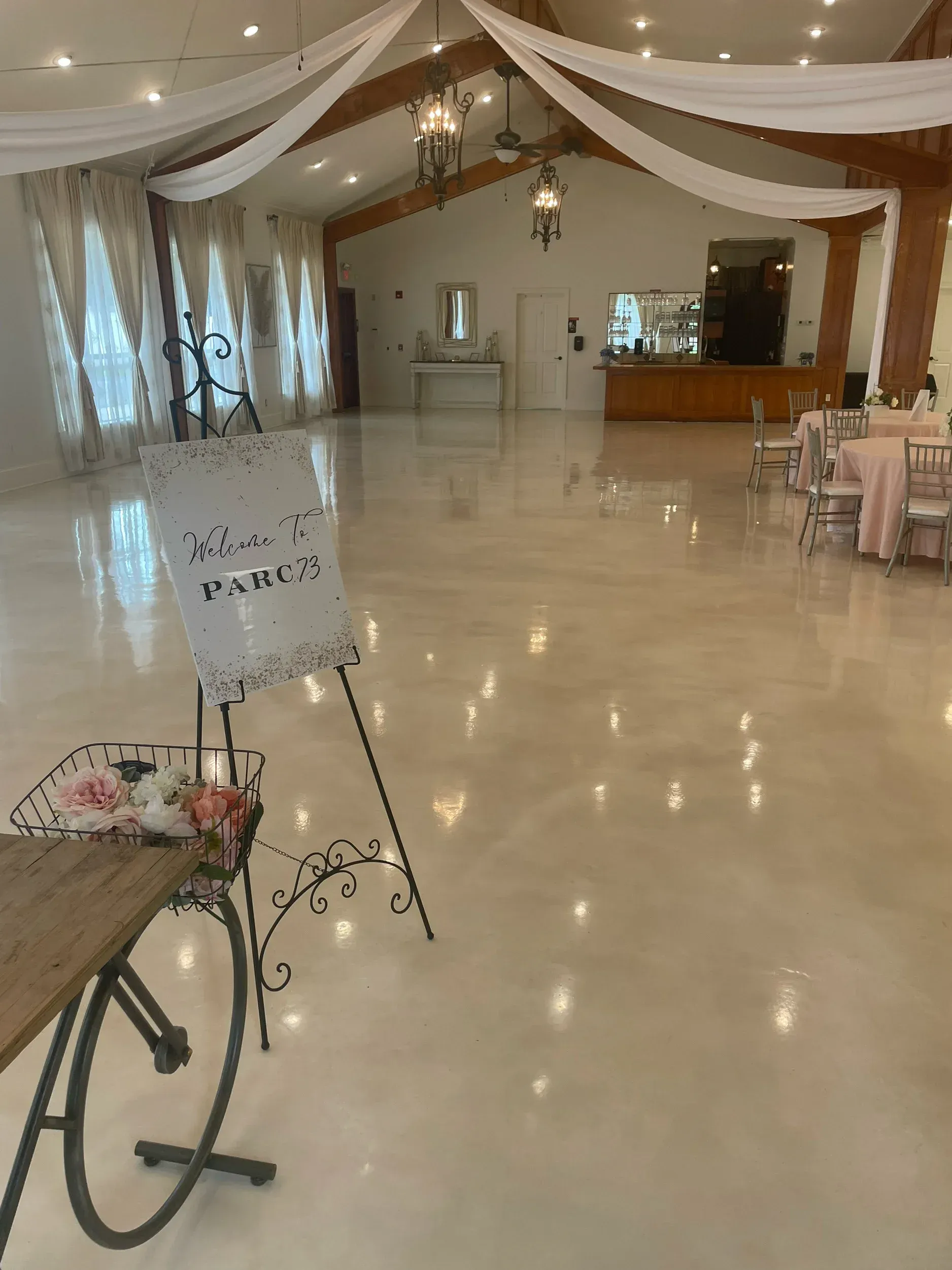 Decorated banquet hall with draped ceiling, polished floor, tables, and a welcome sign by the entrance