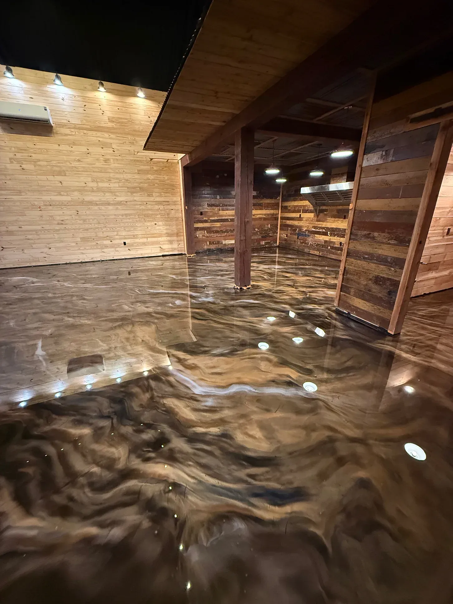 Metallic epoxy floor with wood panel walls. Brown and gold swirls reflect light from ceiling fixtures.