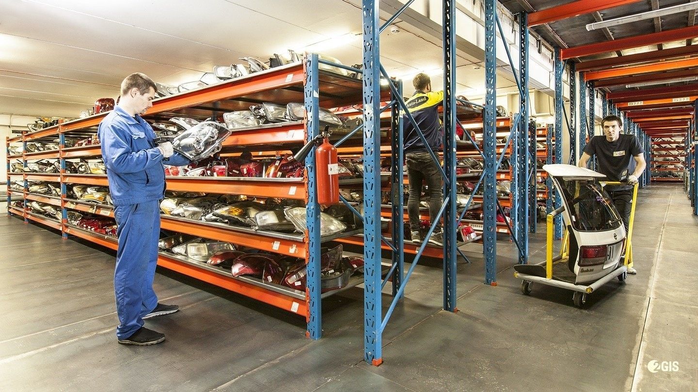 Workers inspecting shelves in a warehouse aisle beside a pallet jack