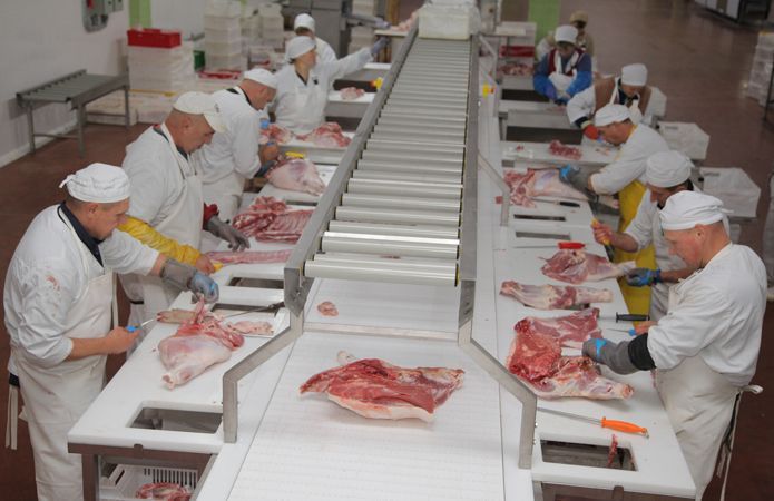 Workers in white uniforms cutting meat on a conveyor line in a food processing plant