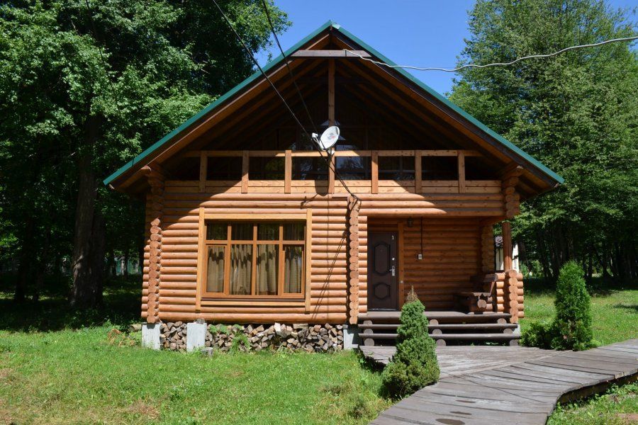 Wooden cabin with a stone path, green lawn, and trees in a sunny forest setting