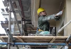 Construction worker in yellow hard hat working on scaffolding beside a building wall