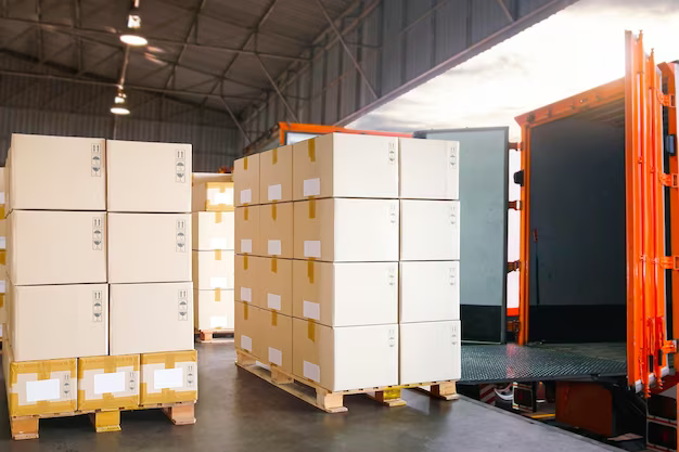 Pallets of boxed goods in a warehouse beside an open orange shipping container