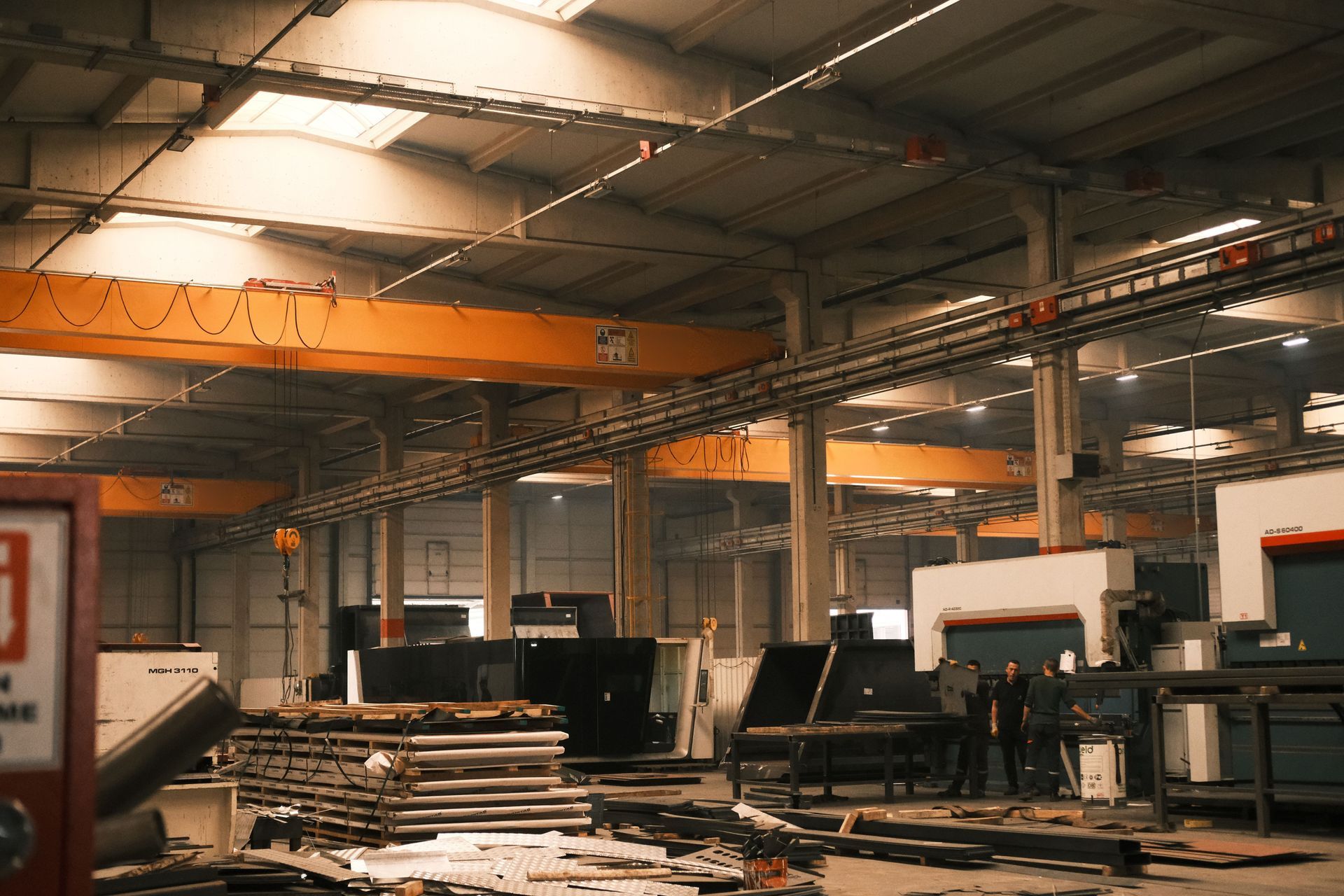 Warehouse worker in orange hard hat checking boxes on a high shelf beside coiled yellow hoses