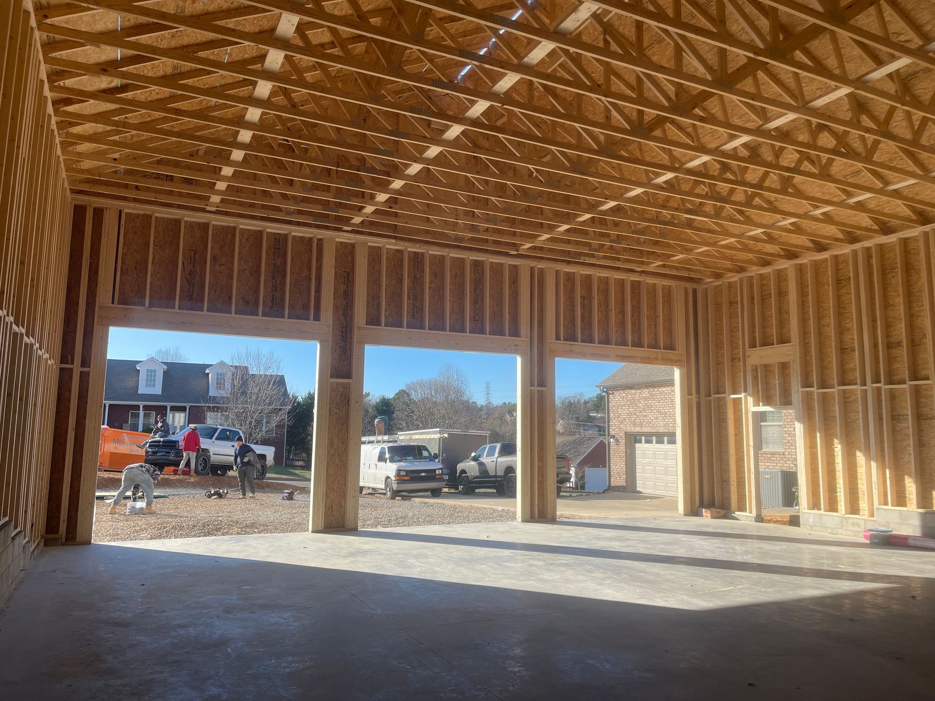 Interior of a wooden building under construction, with workers and trucks visible through open framing.