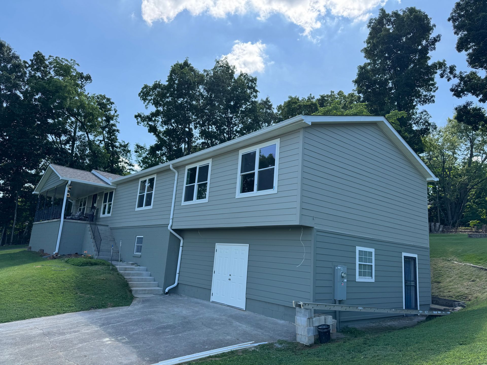 Two-story gray house with white trim, a garage, driveway, and trees under a blue sky.