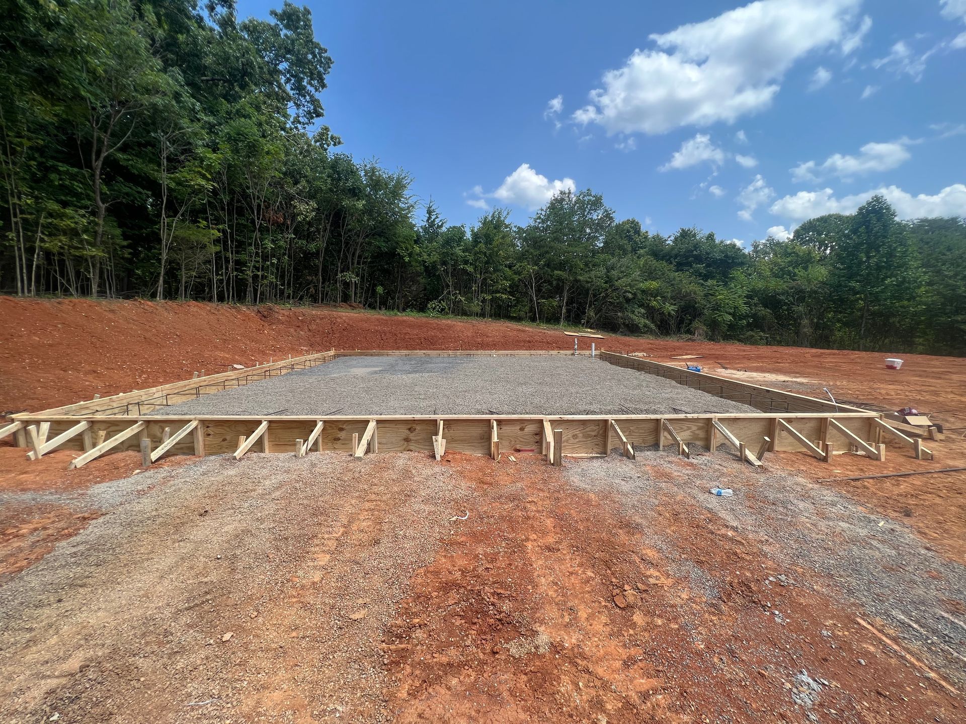Concrete foundation slab under construction on a graded lot, with wooden forms and forested hills in the background