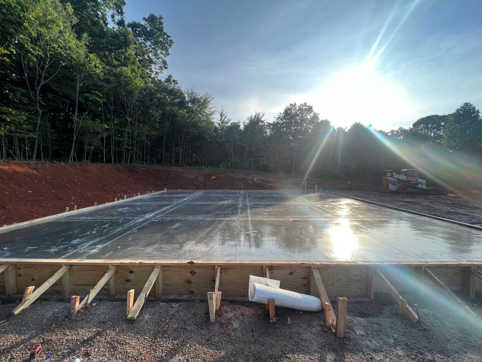 Fresh concrete slab with wooden formwork and a bright sun flare in a wooded construction site